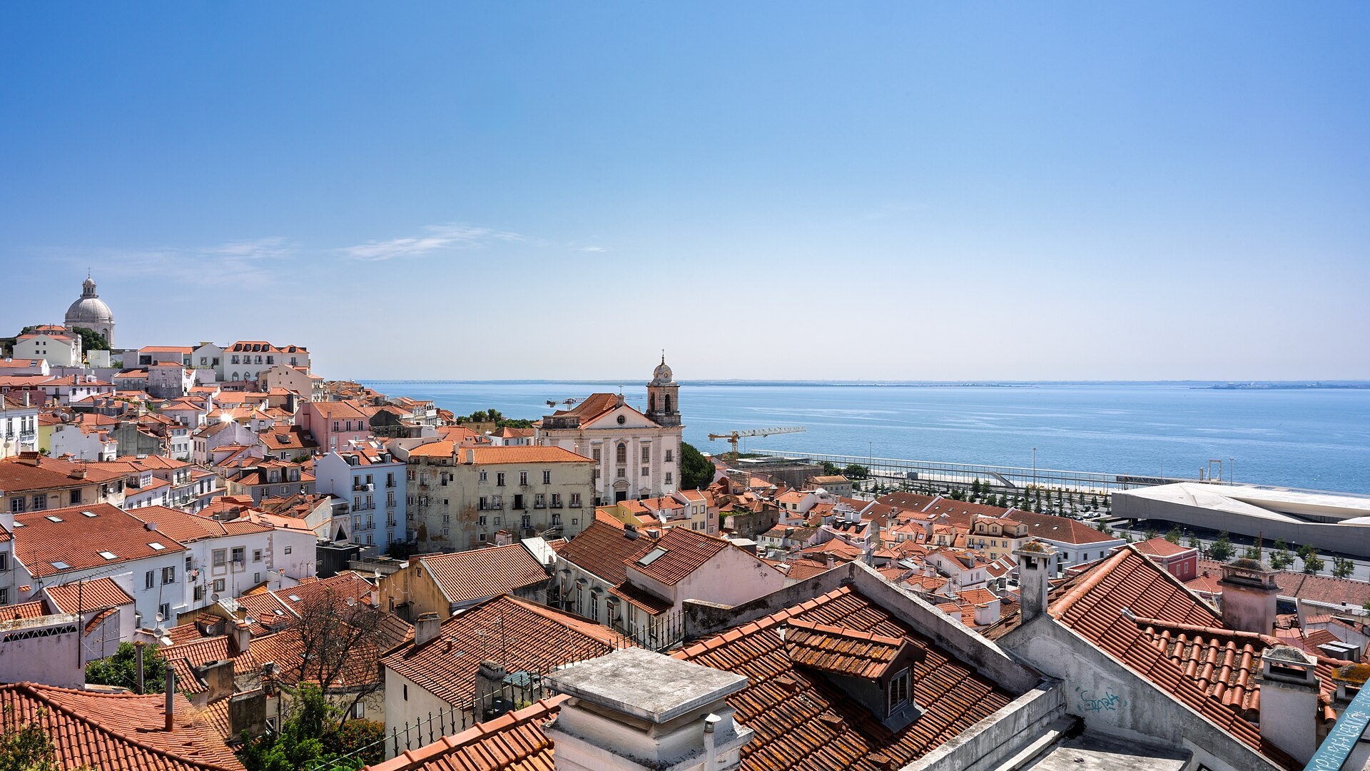 Looking out over the Alfama district in Lisbon, the view reveals a cascade of terracotta rooftops leading down to the shimmering Tagus River
